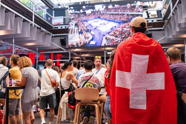 Visiteur portant un drapeau suisse regardant les compétitions olympiques sur un écran géant à la Maison Suisse.