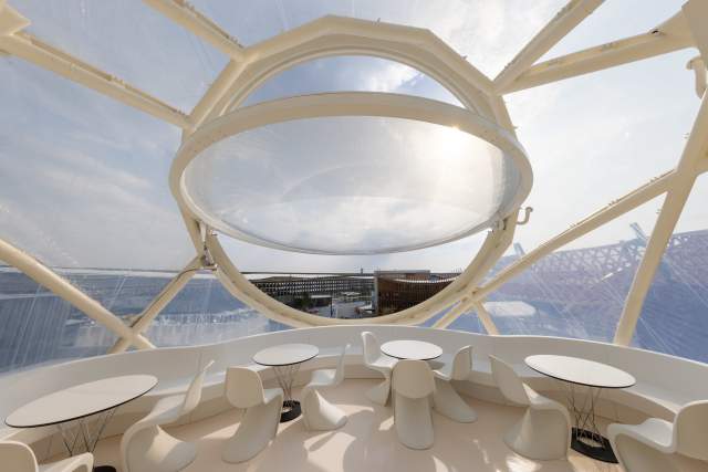 Bright interior of the Swiss Pavilion with a suspended circular structure overlooking the Expo site.