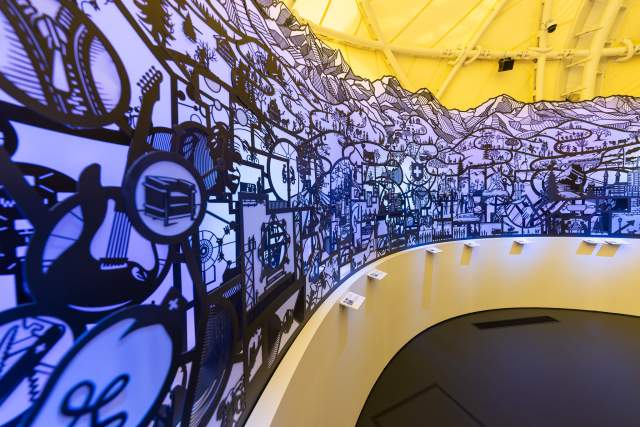 Interior of the Swiss Pavilion featuring black illustrated walls and a curved exhibition space.