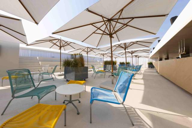 A bright rooftop lounge at the Swiss Pavilion, featuring modern seating and large sun umbrellas.